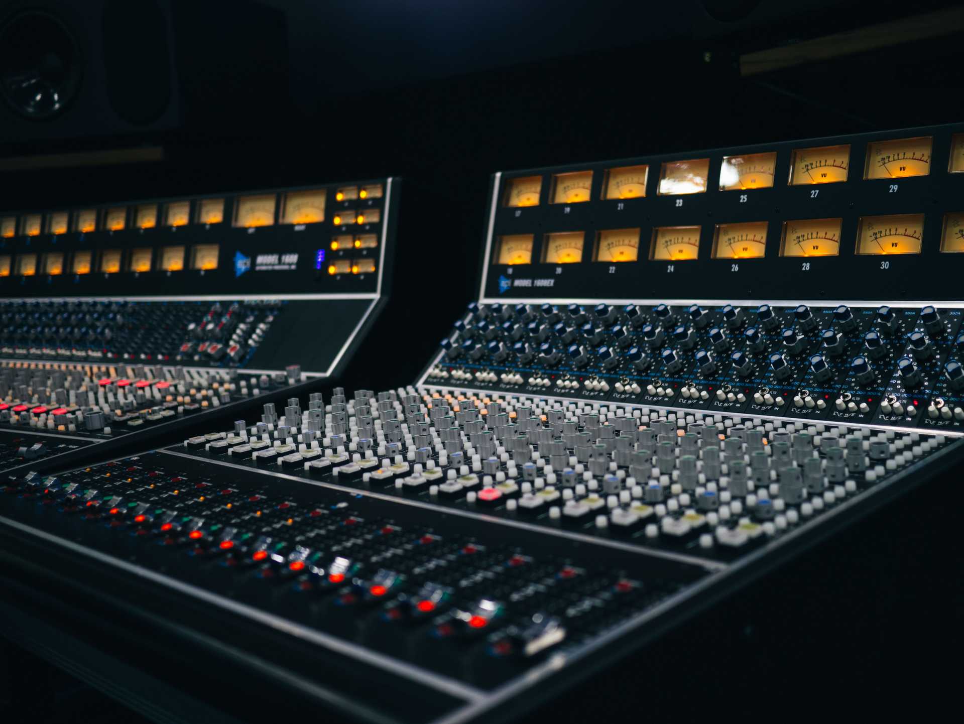 Two mixing consoles displaying VU meters, lots of knobs, and faders.