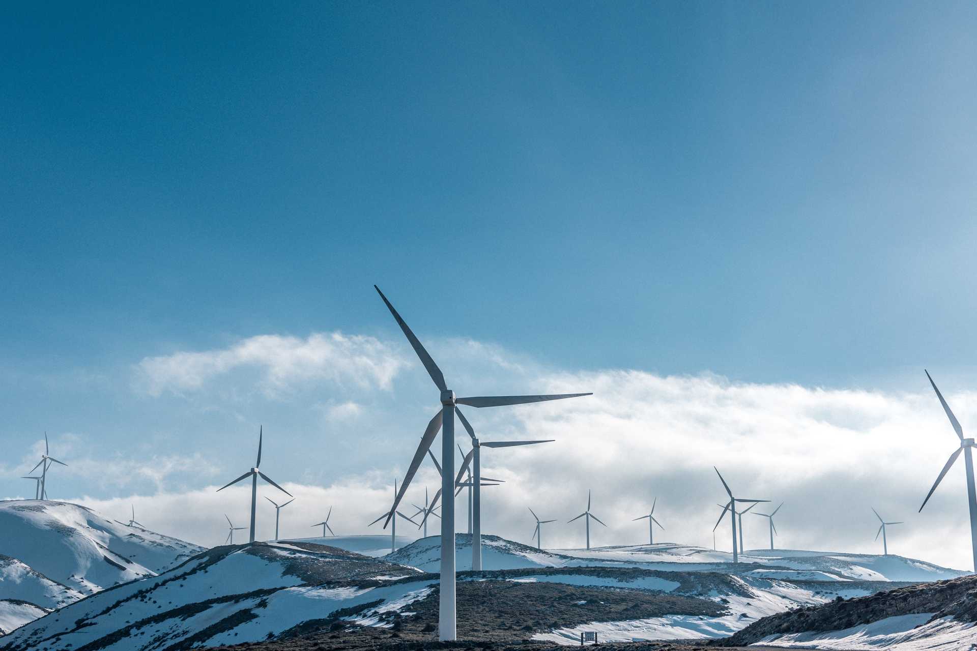 Wind turbines in a snowy area with a sky that is half blue and half clouds.