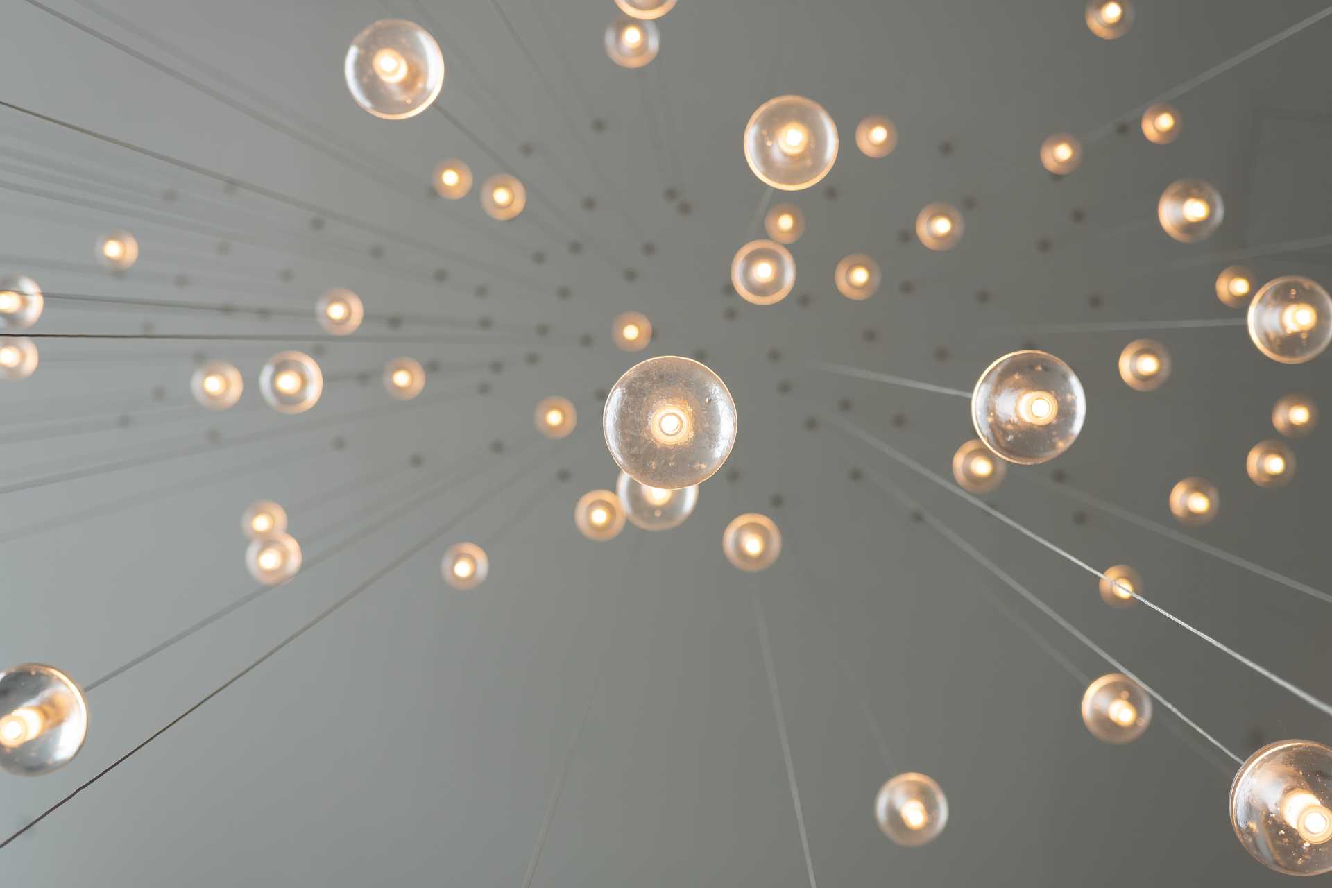 A view from below of spheres with lights connected to long strings hanging from the ceiling.