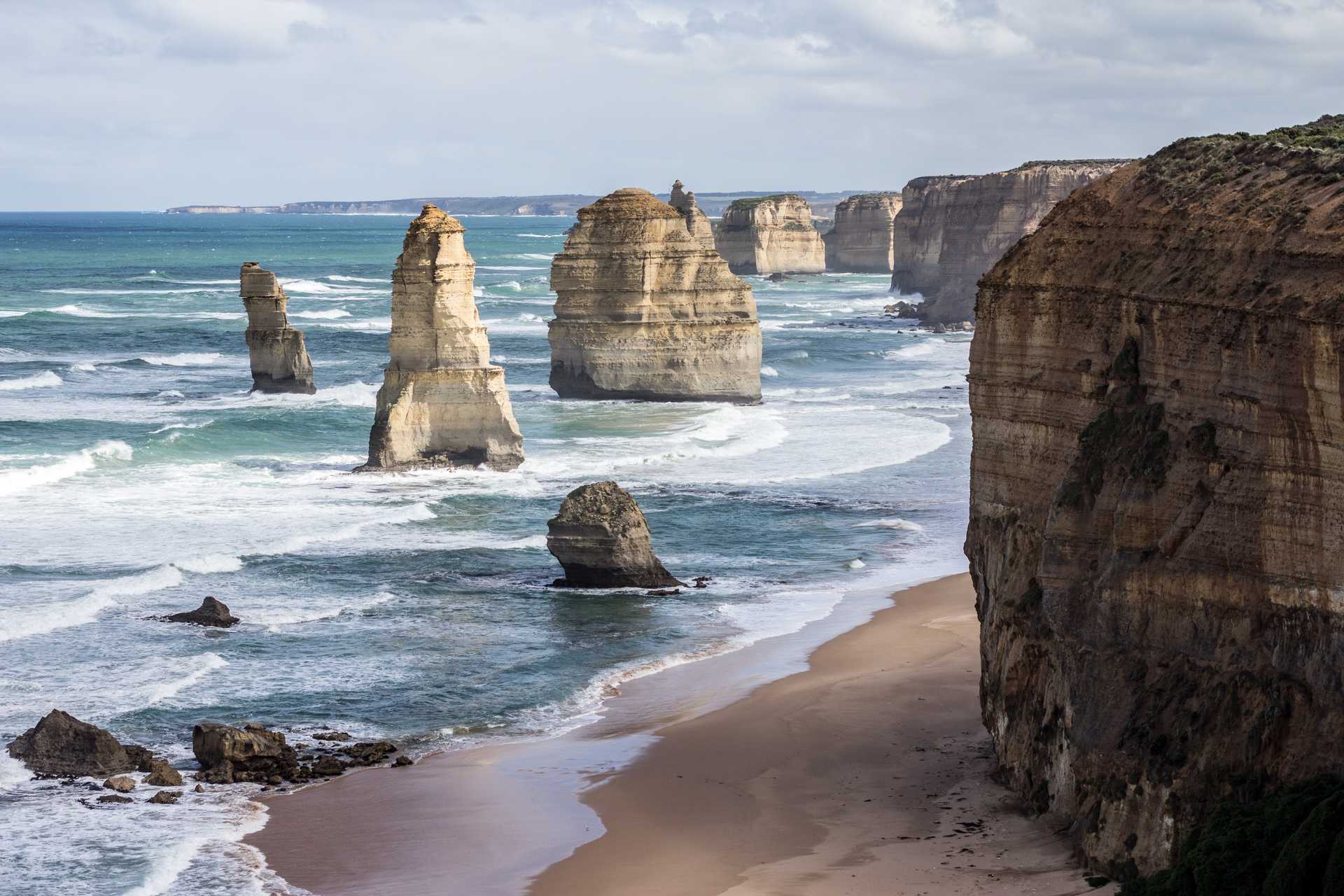 The rock formation known as the twelve apostles. Ocean waves passing huge rock formations and ending on a tranquil beach.