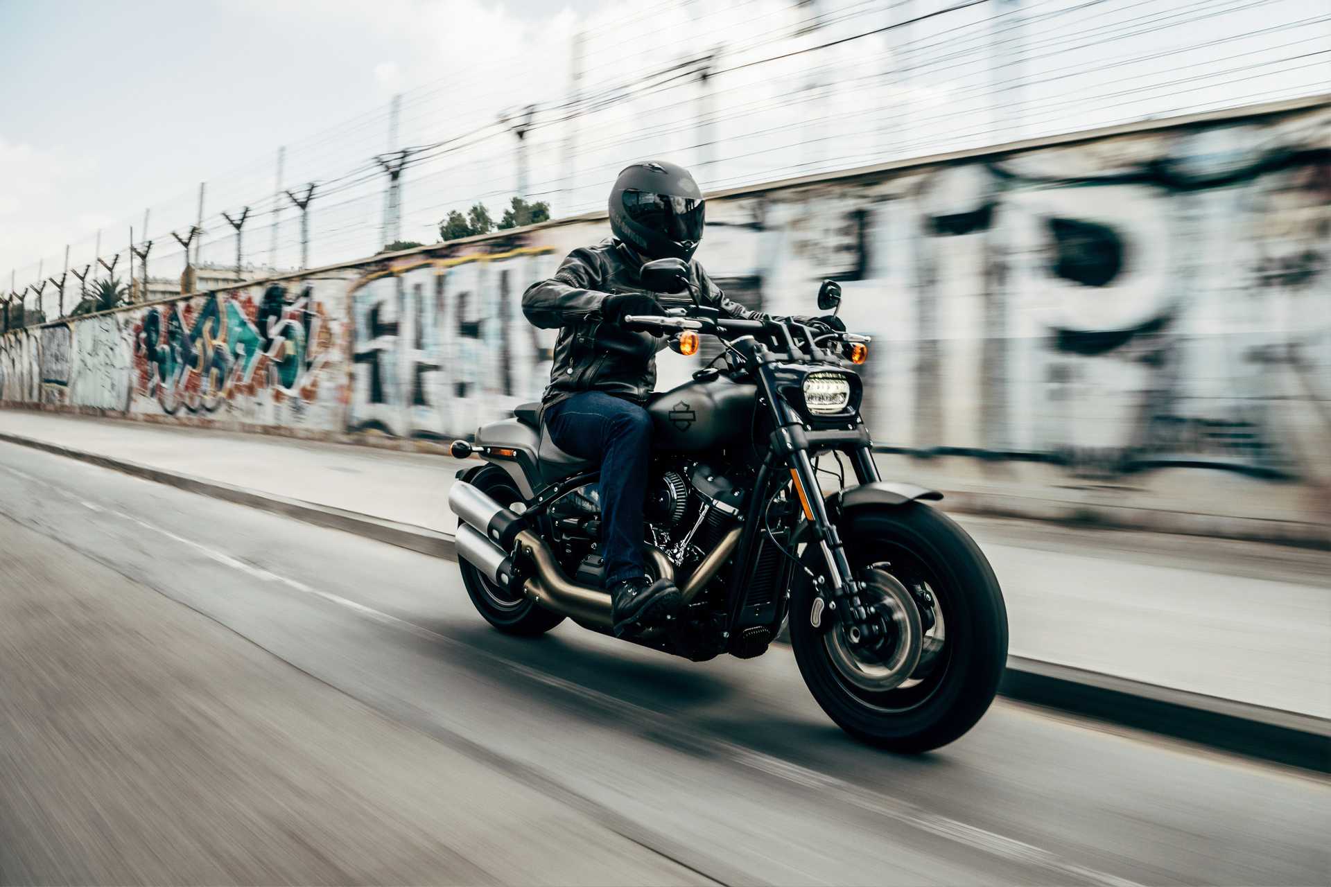 Motorcycle riding down a street with graffiti in the background