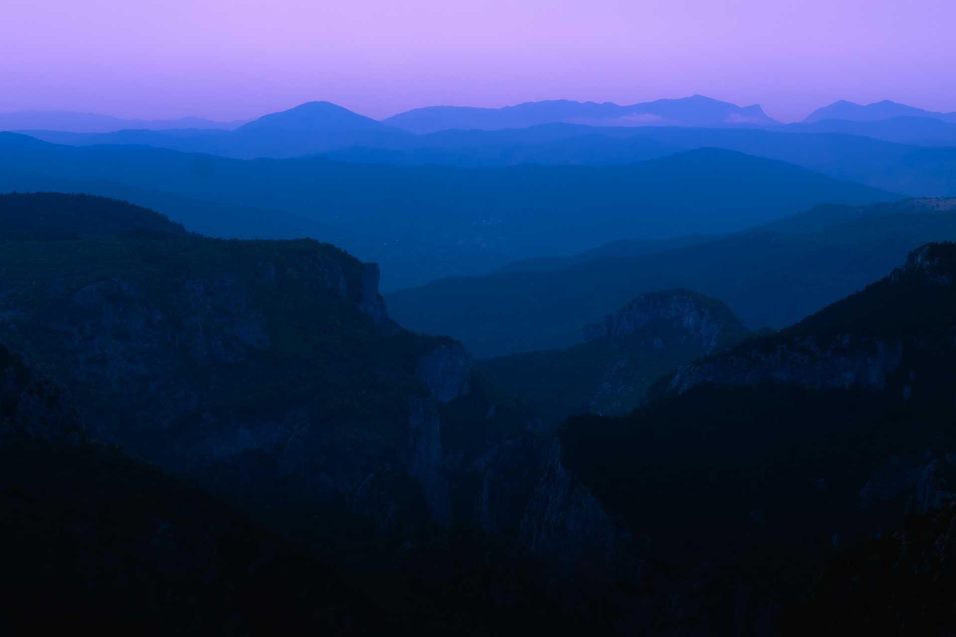 Mountains stretching off into the distance at dusk, the sky goes from dark blue to light purple in the distance