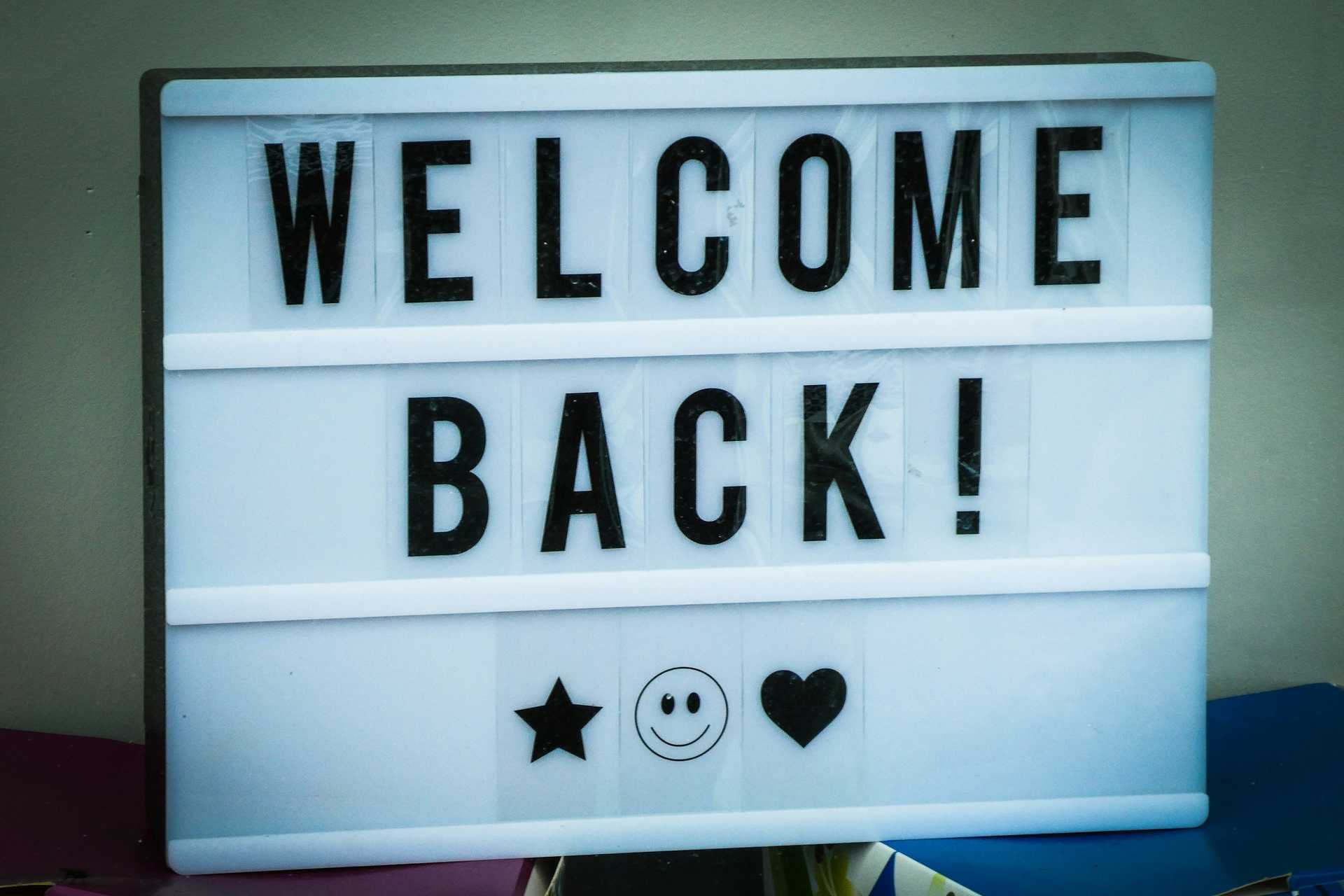 a welcome back sign with a star, smiley face, and heart