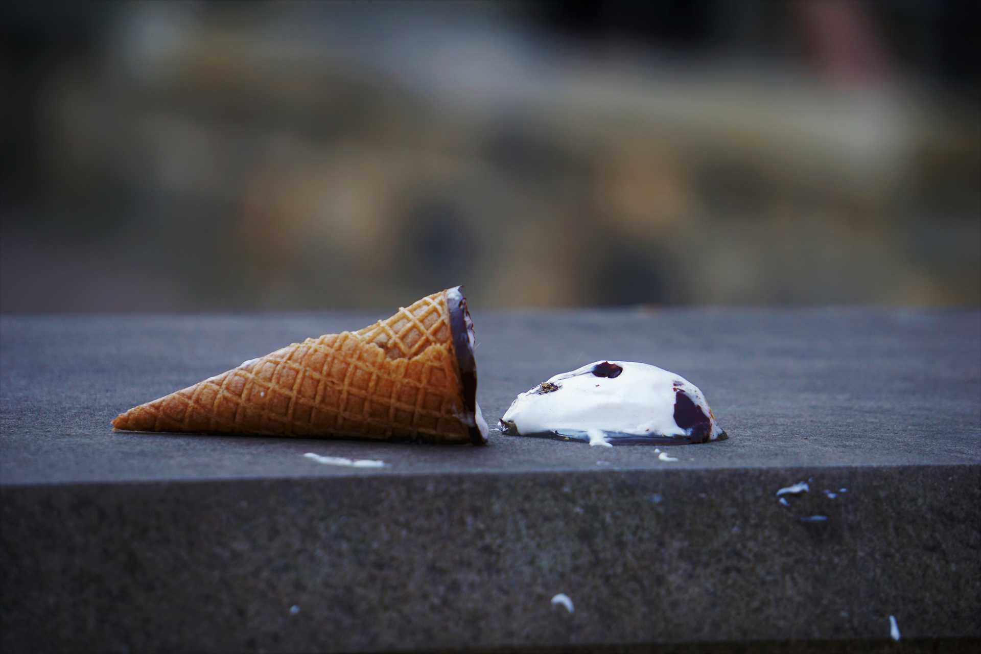 A sugar ice cream cone that is lying on the ground, a dollop of ice cream that appears to be vanilla with brownies in it lying next to it.