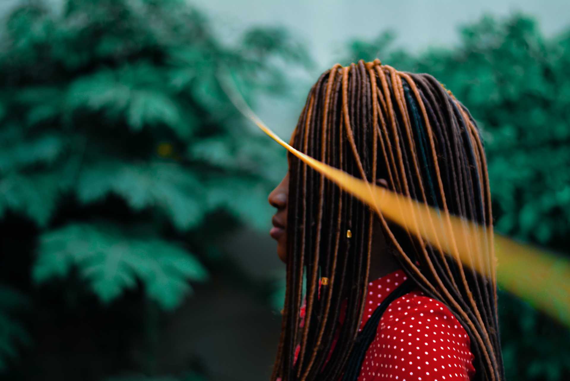 Stylish woman with multi-colored braids against a green forest background