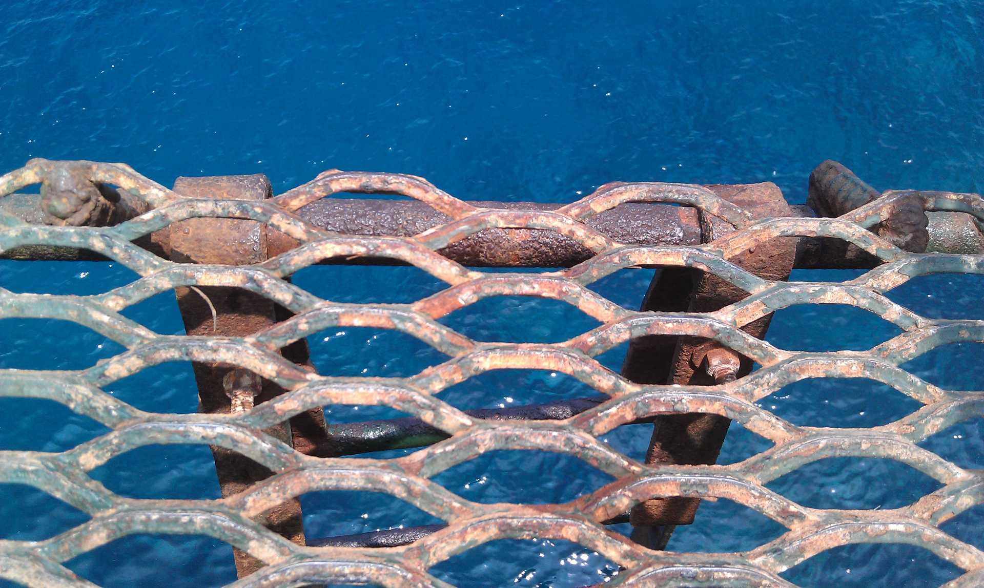 A metal platform of linked six sided matrix at the top of a ladder overlooking the blue ocean.